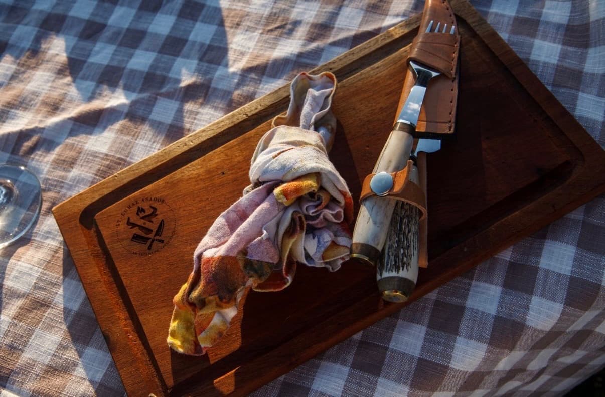 A wooden serving board branded with the St Lumaz Asados logo, an artisan knife resting beside it