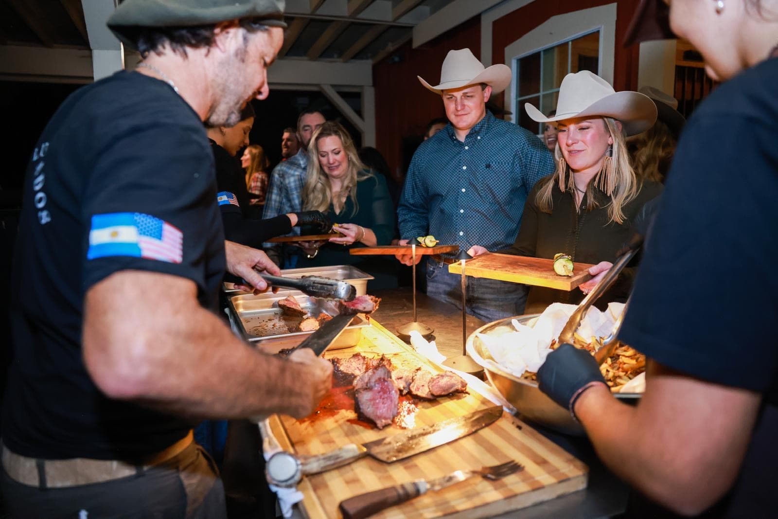 Marcos carving prime beef onto guests' wooden serving boards at an evening asado