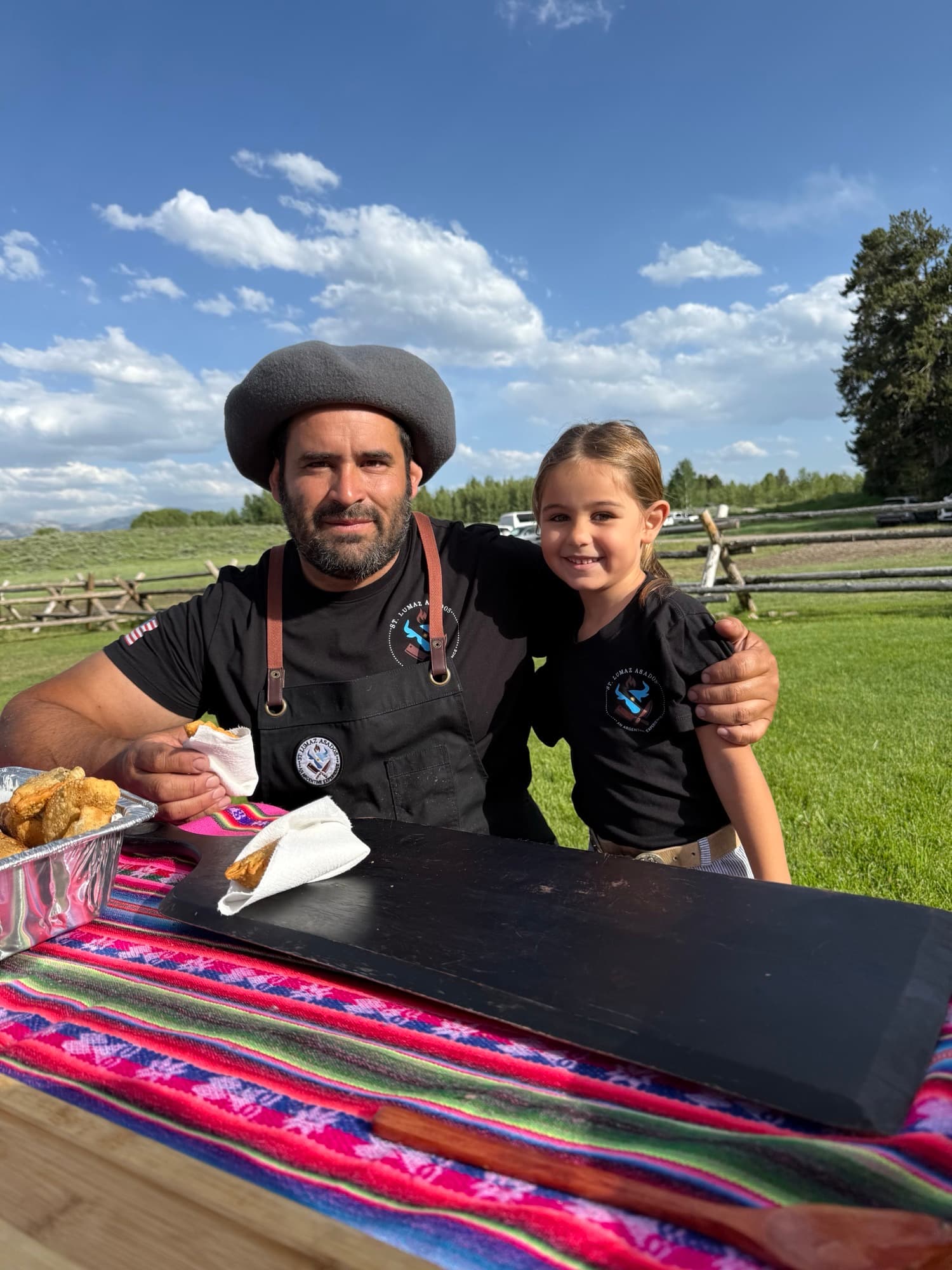 Pancho and a young guest sharing fresh empanadas at the table beneath a big blue sky