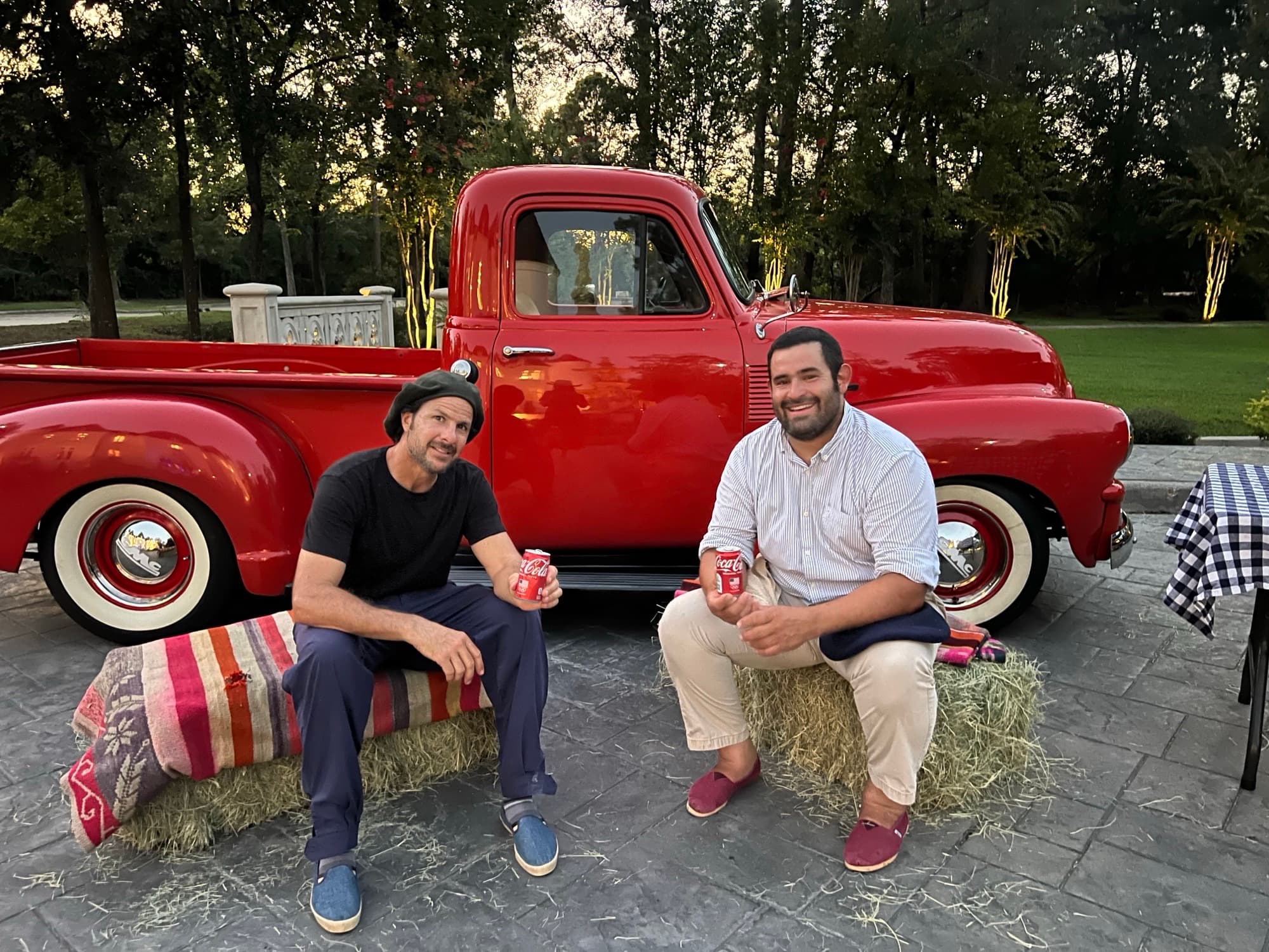 Pancho and Marcos taking a break on hay bales beside a vintage red pickup truck