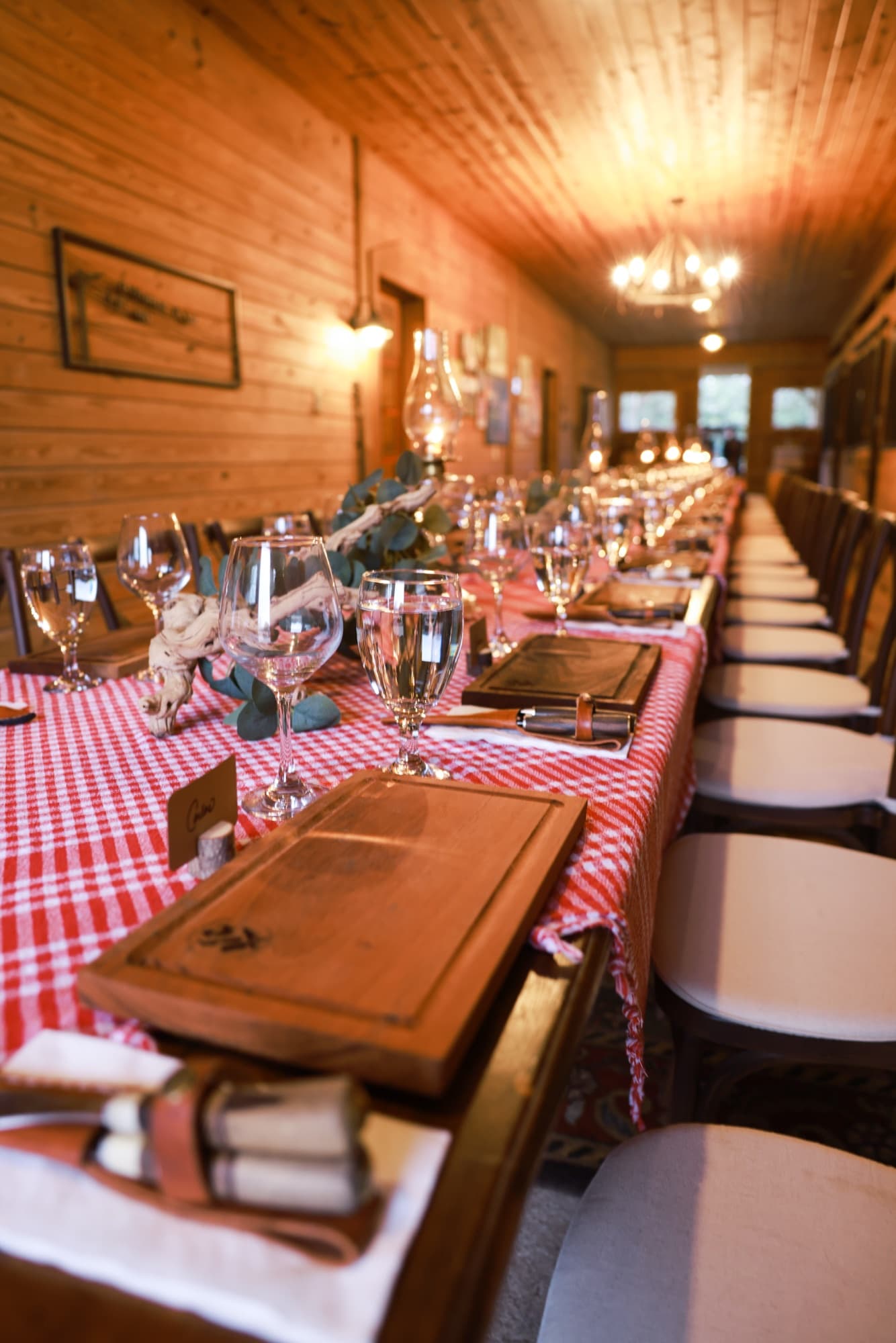 A long communal table set with wine glasses and wooden serving boards inside a warm wood cabin